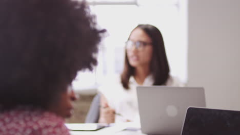 Young-black-woman-making-notes-in-a-meeting-while-her-colleagues-are-talking,-rack-focus,-tilt-shot