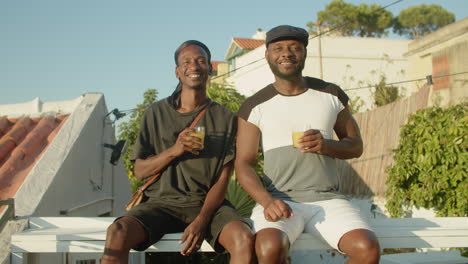 vista frontal de gays felices tintineando vasos y besándose al aire libre