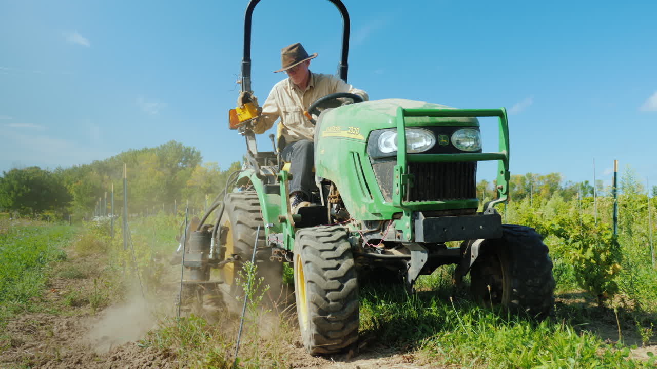 한 농부가 작은 트랙터로 포도원 근처에서 잡초를 뽑고 있다