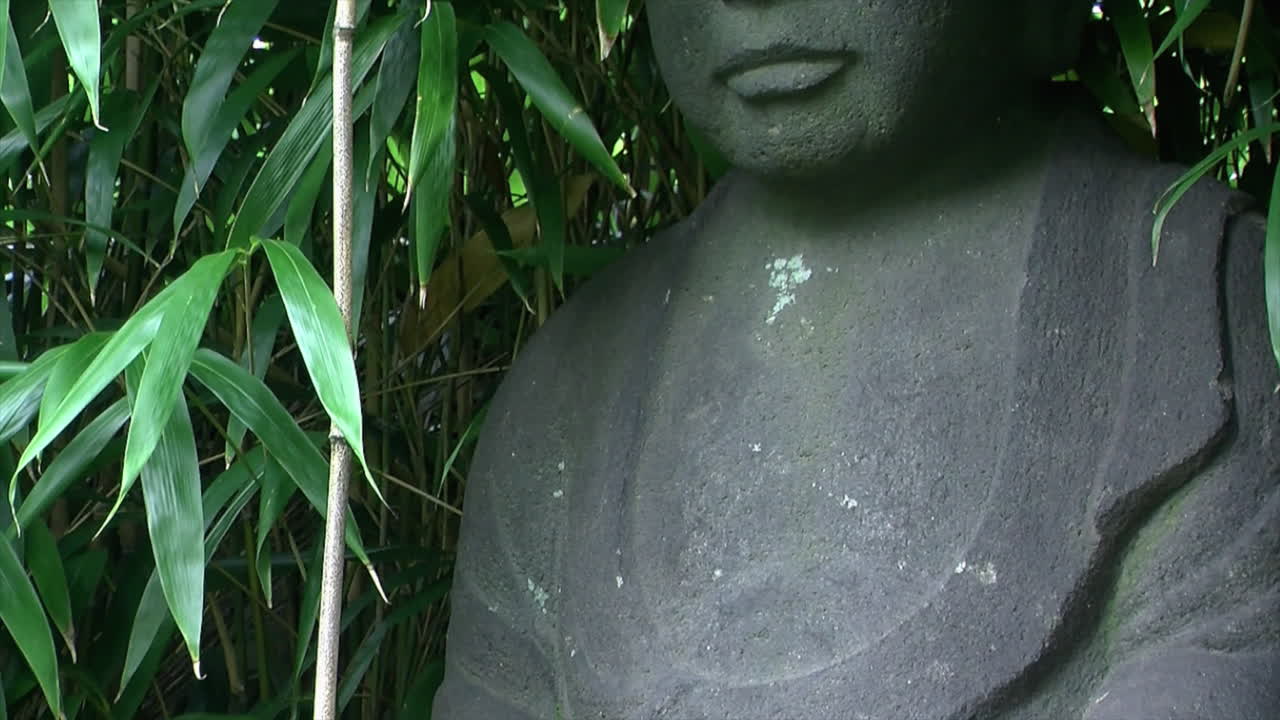 incline hacia arriba de las manos a la cara de la estatua de jizo en un jardín japonés