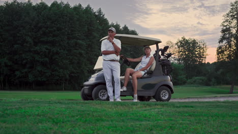 Two-golfers-rest-outdoors-on-golf-course.-Married-couple-relax-in-golf-cart.