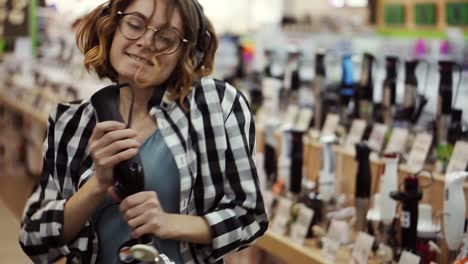 Portrait-of-cute-caucasian-pretty-young-woman-with-short-curly-hair,-plaid-shirt-and-in-headphones-dancing-and-pretending-she's