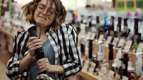 Portrait of cute caucasian pretty young woman with short curly hair, plaid shirt and in headphones dancing and pretending she&#039;s