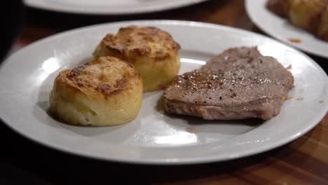 grilled steak dish with potatoes cakes being added to the dish