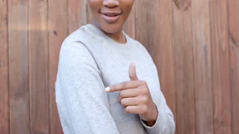 Happy-african-american-woman-in-grey-sweatshirt-pointing-to-sleeve,-slow-motion,-copy-space