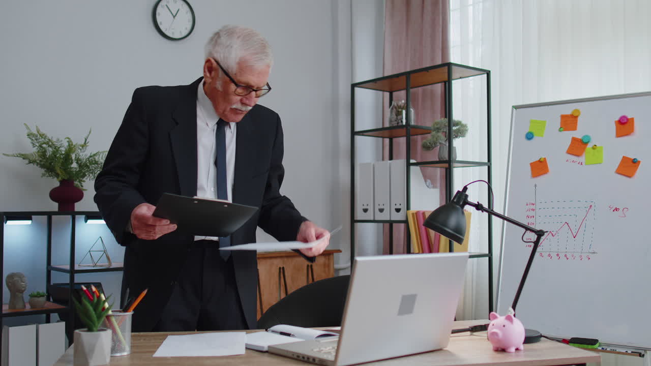 Senior business man examining graphs, analyzing, managing finance documents report at home office