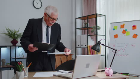 senior business man examining graphs, analyzing, managing finance documents report at home office