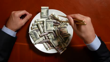 hands of a businessman with chopsticks and dollar rolls. eating dollars. 4k.