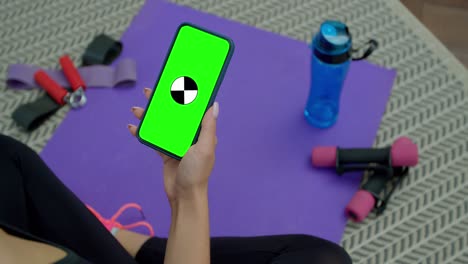mujer de fitness cansada usa teléfono inteligente con pantalla verde después de entrenar en casa. entrenamiento, entrenamiento, bienestar, concepto deportivo.