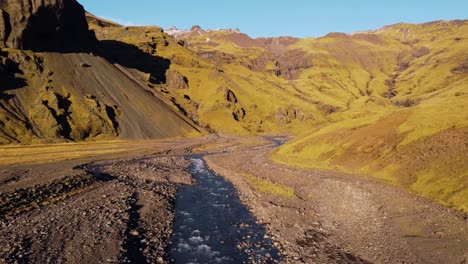 a breathtaking view captures a deep, winding canyon with dramatic, multi-toned walls carved by a dark river under a clear blue sky, showcasing iceland's raw geological beauty