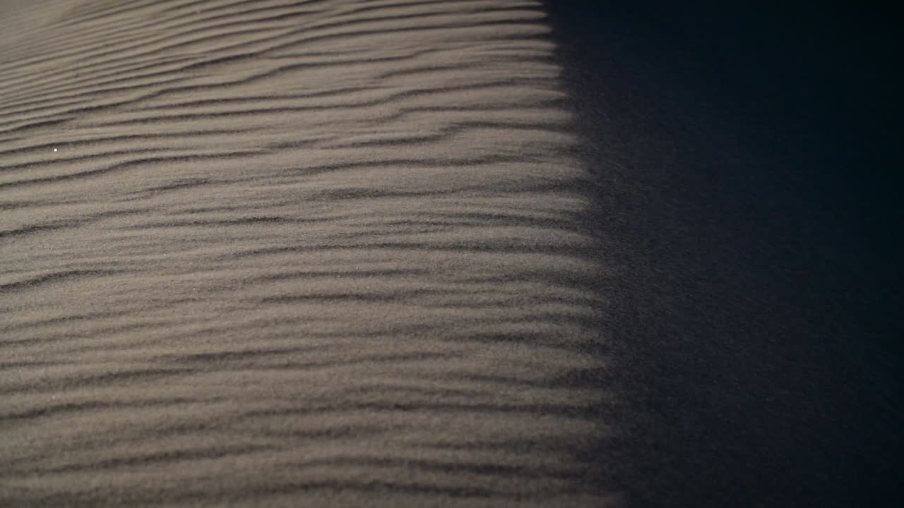 Sand blows over a sand dune with deep shadows