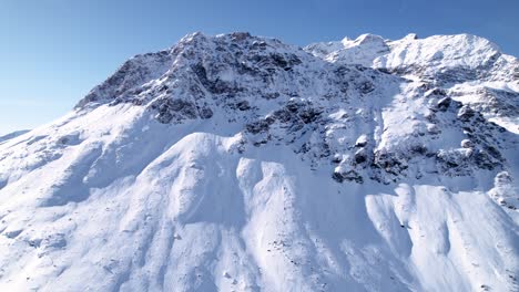 Vista-Aérea-Del-Paisaje-Montañoso-Cubierto-De-Nieve-Con-Bosques-En-Un-Soleado-Día-De-Invierno-En-Alp-Grum,-Suiza