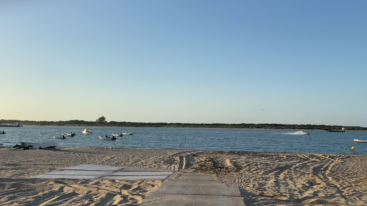 Awan berwarna oranye lembut dan ungu menghiasi langit di atas Samudra Atlantik saat cahaya terakhir memudar di atas pantai Sanlúcar