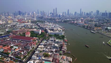aerial establishing overview of the chao phraya river in bangkok, thailand, showing boats, city skyline, and waterfront with dazzling red rooftops and bustling waterway