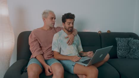 two men relaxing on a couch, using a laptop