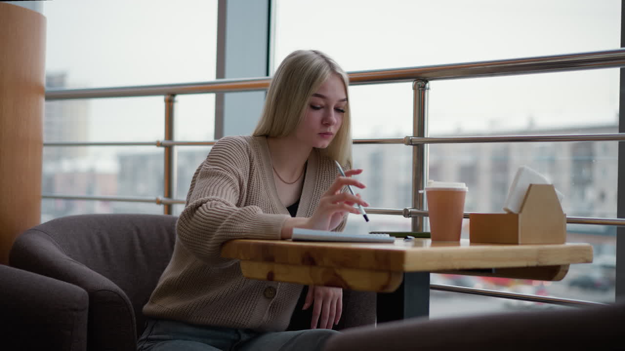 dama profundamente pensativa, tocando la pluma en el papel mientras bebe café, reflexionando o haciendo una lluvia de ideas en un acogedor café, taza de café en la mesa, atmósfera relajada
