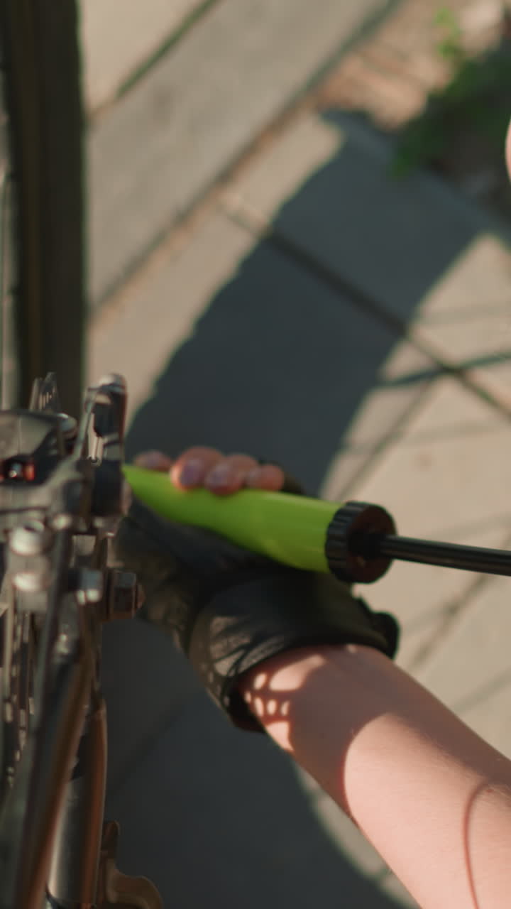 primer plano de una mujer con guantes bombeando aire en un neumático de bicicleta con boquilla verde en un día soleado, con enfoque en su mano y bomba, fondo suavemente borroso