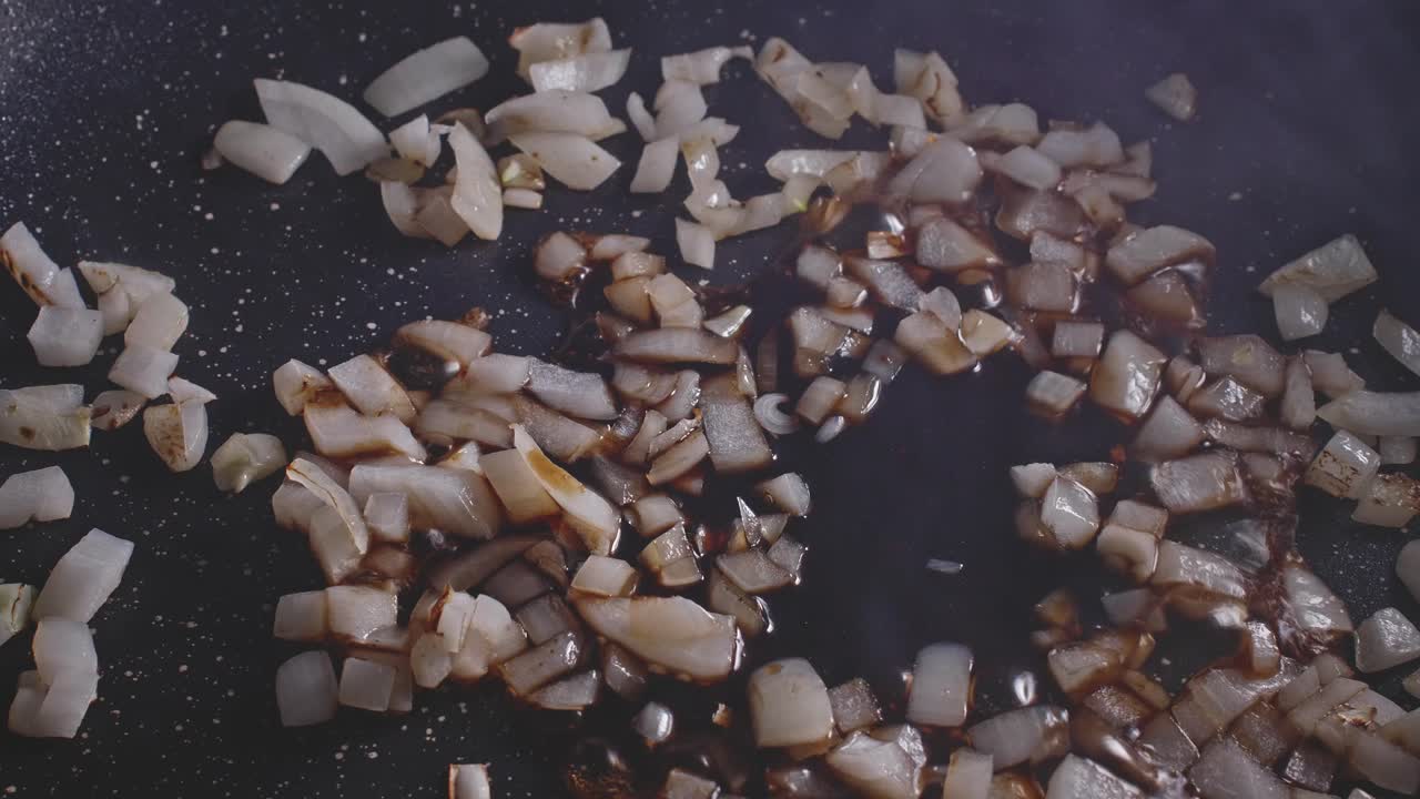 Adding soy sauce and tomato sauce to chopped onion veing cooked on a frying pan, then mixing it all with a wooden spoon, very close up view