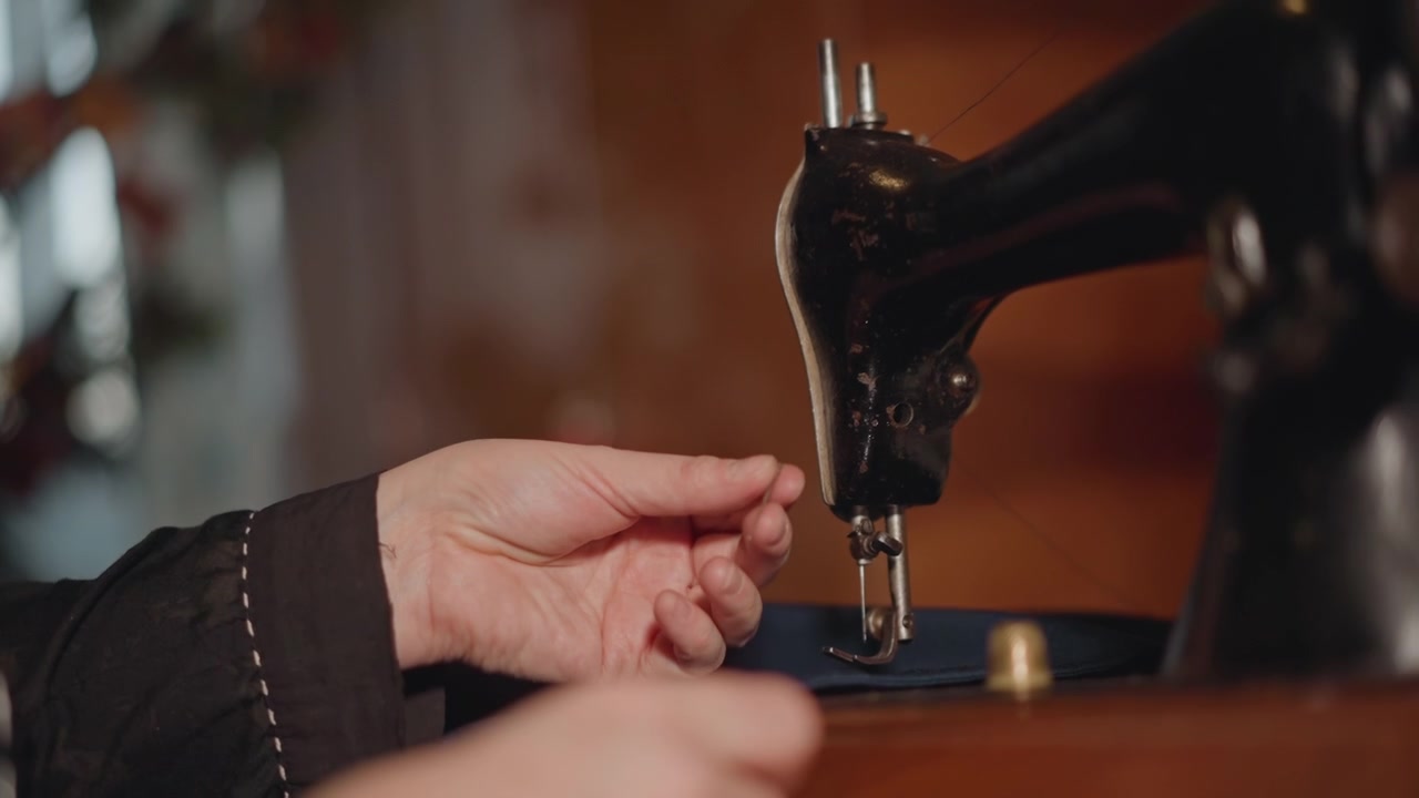 Artigiano cuce pazientemente tessuto vintage. Artigiano guida con perizia il tessuto attraverso un'antica macchina da cucire. Sarto concentrato usa mano ferma per cucire il materiale su un vecchio apparecchio da cucito in metallo.