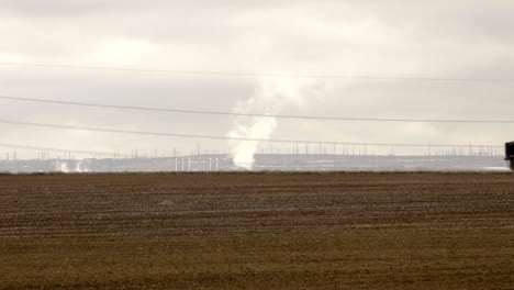 Dump-truck-driving-left-to-right-on-rural-road-in-arid-farm-landscape,-static-long-shot