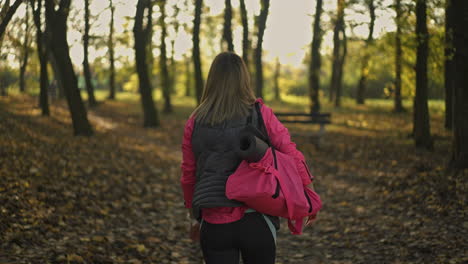 woman walking with yoga mat and gym bag in an autumn park