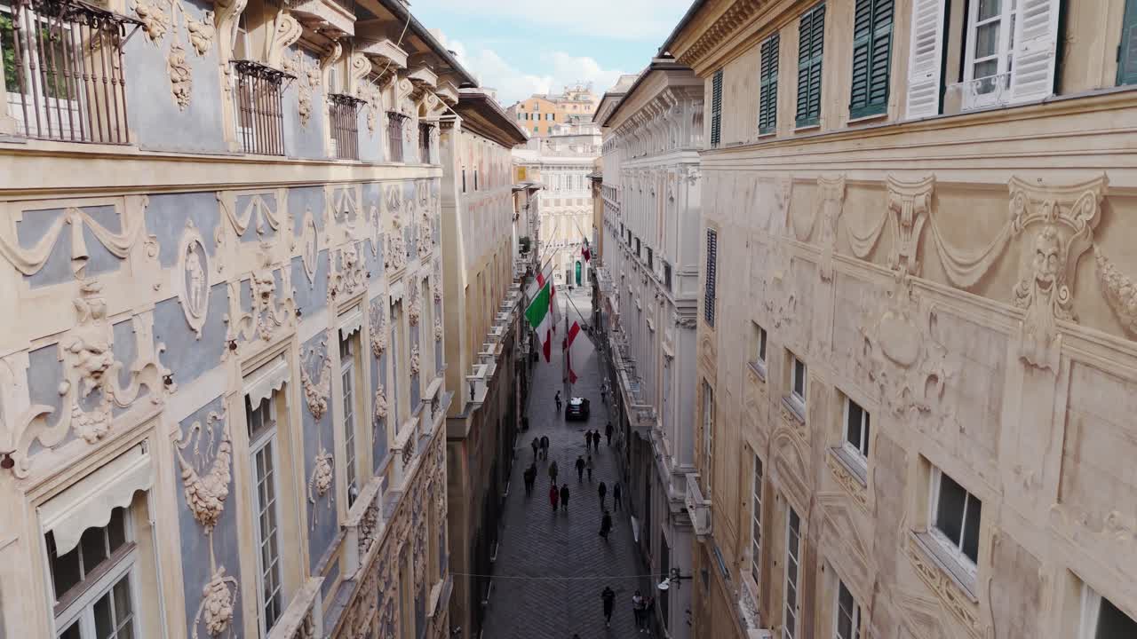 Tourists stroll through a narrow street in Genoa's historic center, lined with ornate old buildings