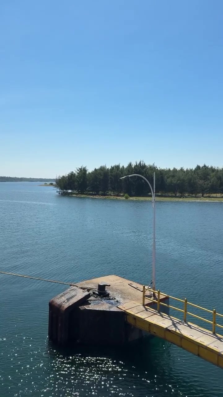Small Pier on Calm Blue Water with Forested Shoreline Under Clear Sky
