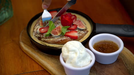movimiento lento de una hembra cortando un rollo de canela cubierto de higos cortados y fresas en una sartén de hierro acompañado de crema batida y salsa