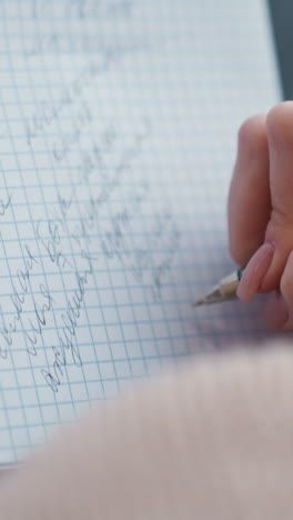 primer plano de la vista trasera de la señora escribiendo en el cuaderno, centrándose en la mano sosteniendo el bolígrafo y la escritura a mano en papel cuadrícula. enfoque suave en la mano mientras escribe con concentración