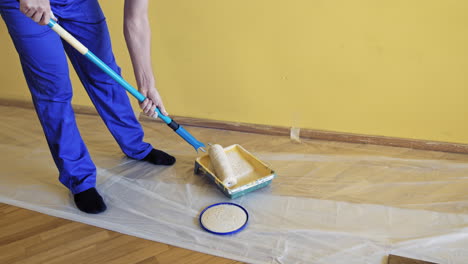 worker get paint on a roller paint before the renovation. man taking new color on a paintbrush in a paint tray to decorate walls in the apartment.