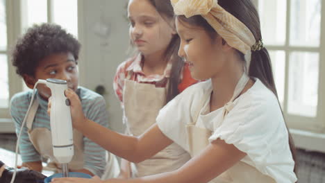 little asian girl using hand blender during culinary lesson