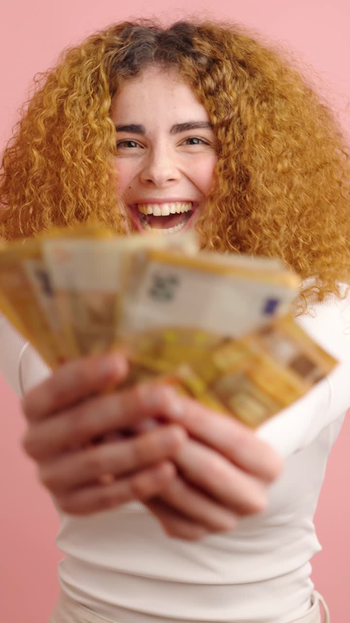 Jonge vrouw die bankbiljetten toont op een roze achtergrond