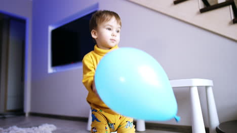 sweet little kid wearing yellow clothes is at home. lovely boy takes a big blue balloon to play.