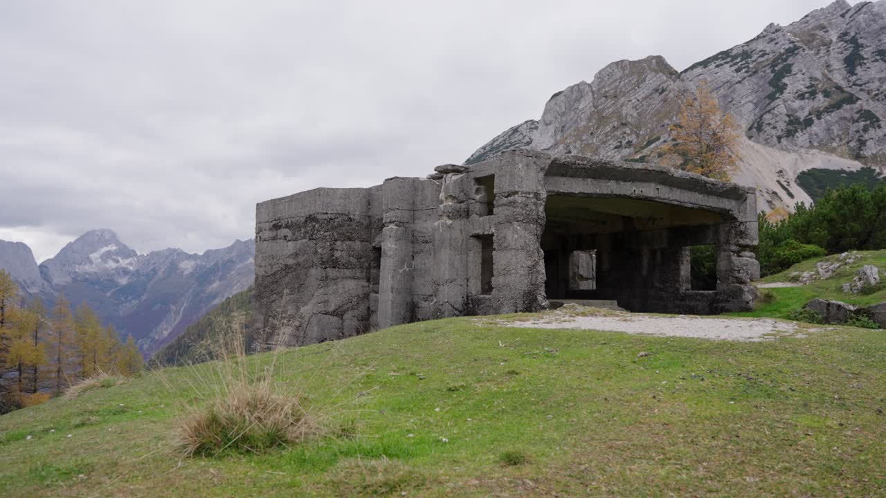 Búnker histórico de la Primera Guerra Mundial en una cresta alpina cubierta de hierba con picos montañosos en el Paso Vrsic, Eslovenia. Toma estática.