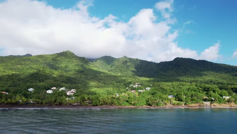 drone flying over ocean waters towards plage de grande anse beach with lush forest in background, guadeloupe