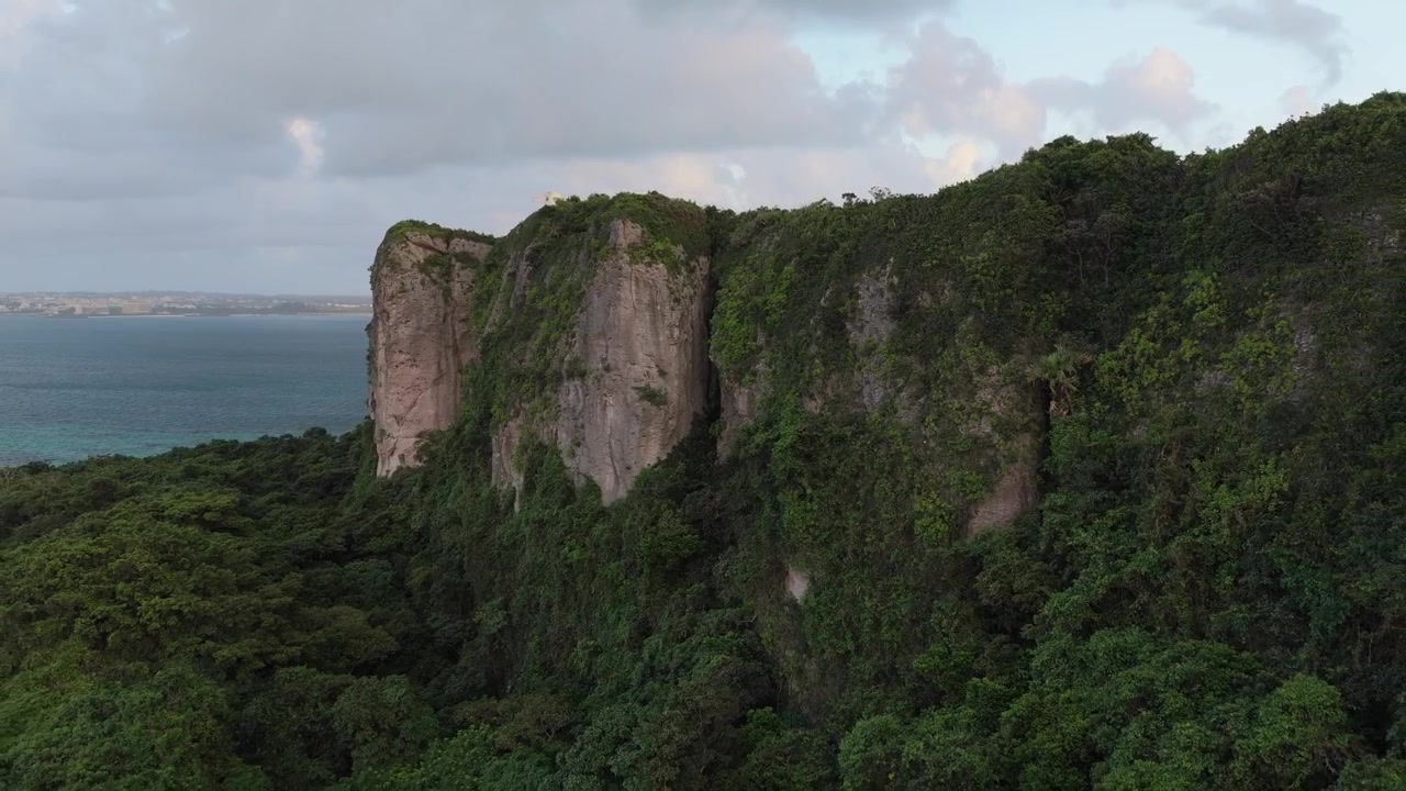 Rekaman udara horizontal yang bergerak mundur dari tebing kapur menjulang tinggi dan hutan lebat Pulau Irabu, Miyako, Okinawa, Jepang, menyingkap pemandangan pesisir yang dramatis