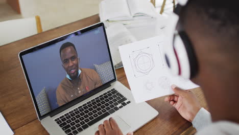estudiante universitario afroamericano que sostiene notas mientras hace una videollamada en una computadora portátil en casa