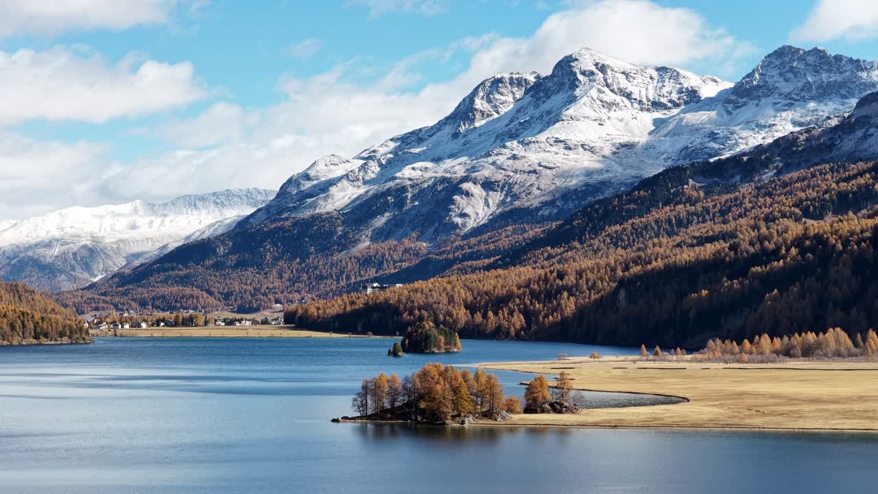 Drone flying forward over Lake Silvaplana with snowy mountains and a small island in Switzerland