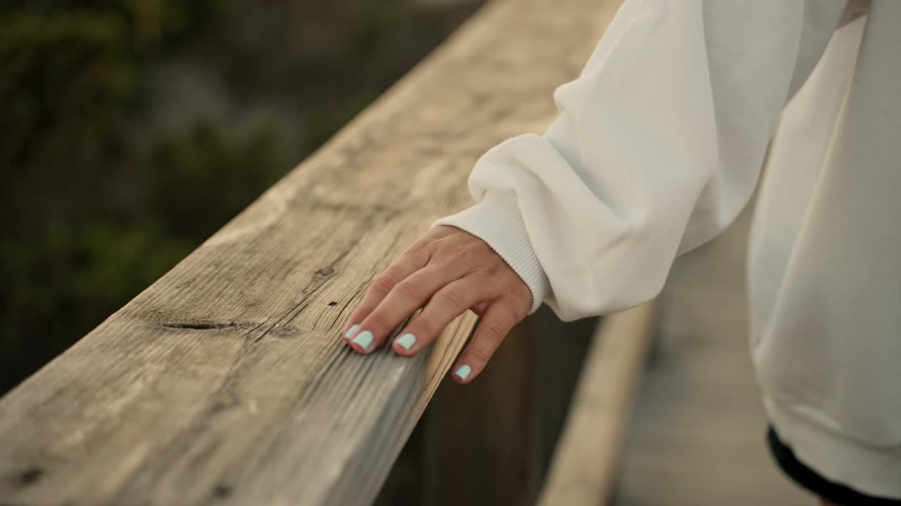 Painted nails woman's hand caressing a wooden handrail walkway