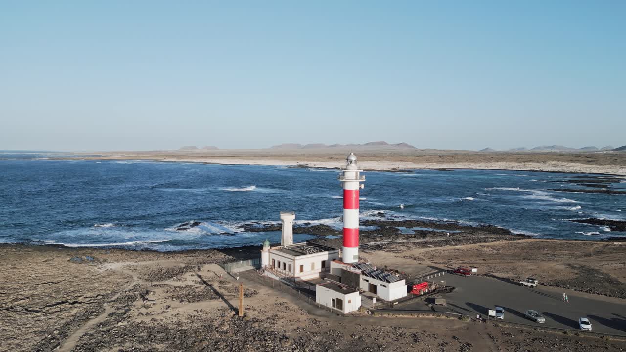 Drone footage circling El Tostón Lighthouse in El Cotillo, Fuerteventura, with rocky volcanic terrain and the Atlantic coastline in view.