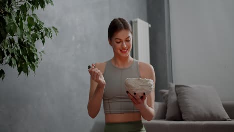 Happy-calm-brunette-girl-in-a-gray-top-and-green-sweatpants-lights-a-special-homemade-aromatic-candle-before-doing-yoga-and-sports-in-a-modern-apartment-at-home