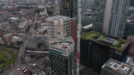 Orbit-shot-around-tall-modern-building-in-process-of-construction.-Tower-crane-on-construction-site.-Aerial-view-of-traffic-in-streets-below.-London,-UK