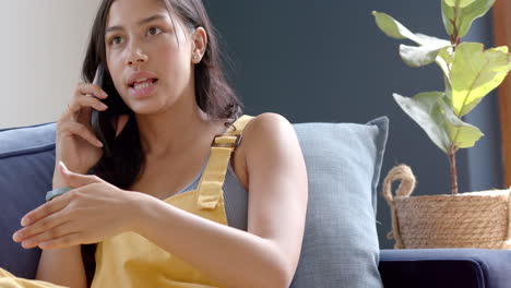 serious biracial teenage girl sitting on couch talking on smartphone, copy space, slow motion