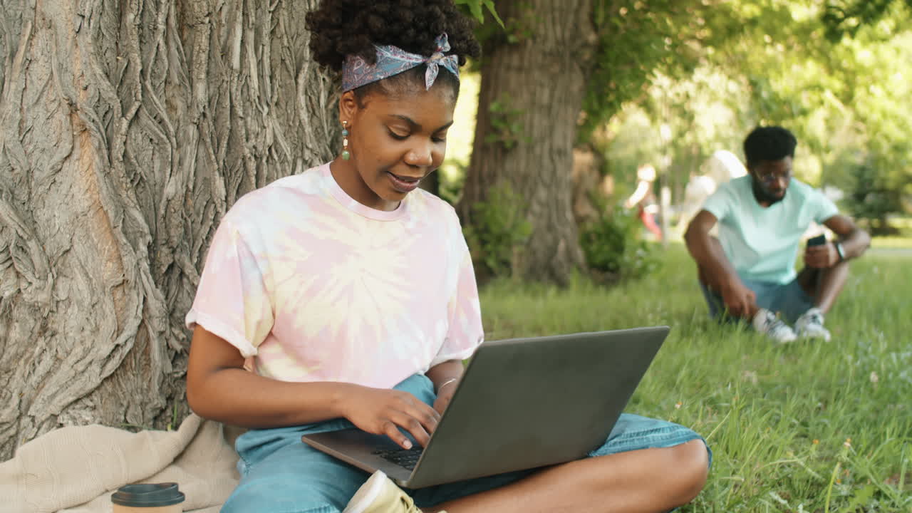 joven mujer afroamericana escribiendo en una computadora portátil en el parque