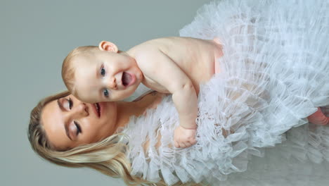 adorable naked baby boy smiling sweetly sitting in mom's hands. mother kisses her beloved son and presses to herself. vertical screen.