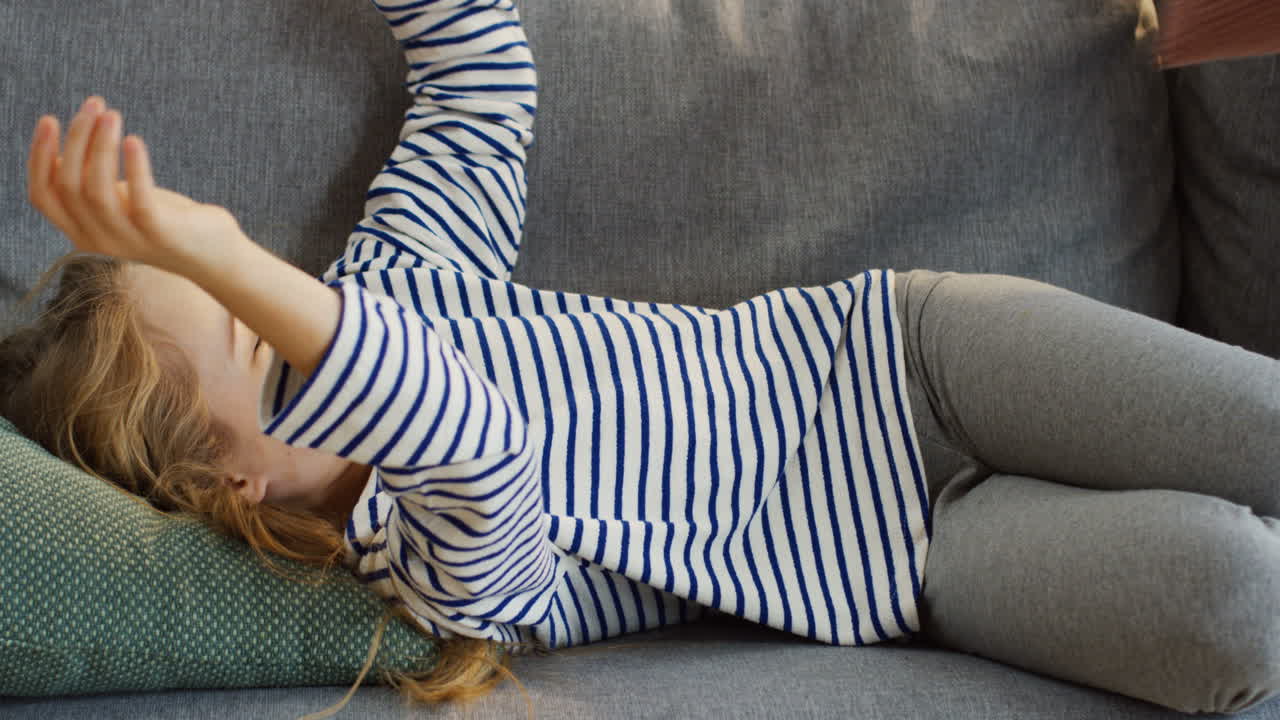 두 명의 작고 재미있는 아이들, 남매, 아늑한 거실에 있는 소파에서 즐거운 시간을 보내고 포옹하고 웃고 있습니다.