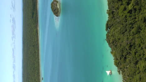 Vertical-aerial-of-Upi-Bay,-with-pirogue-sailing-along-coastline,-Isle-of-Pines