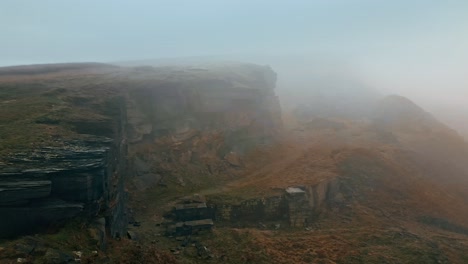 aerial drone view of an clouds moving over standedge edge in the hills, pennines on a foggy morning, golden hills and beautiful rocky cliffs and moorlands