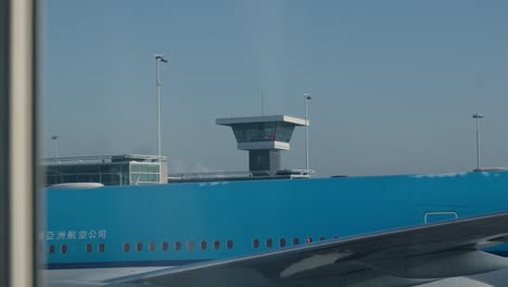 Blaues-Flugzeug-Mit-Dem-Kontrollturm-Im-Hintergrund-Am-Flughafen-Rotterdam-In-Den-Niederlanden