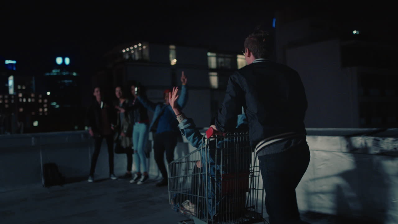 un grupo feliz de amigos jugando con el carrito de compras divirtiéndose en la azotea por la noche disfrutando de la fiesta de celebración del fin de semana